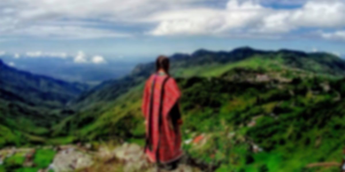 A traveler in a red sarape looking over the green mountains of the Sierra Juárez